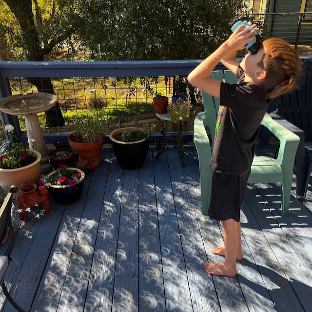 Boy on dark T-shirt and shorts looking through solar binoculars.