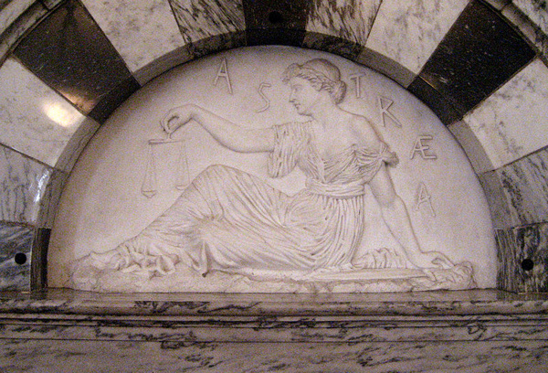 Relief sculpture of sitting woman in Greek garb holding a set of scales.