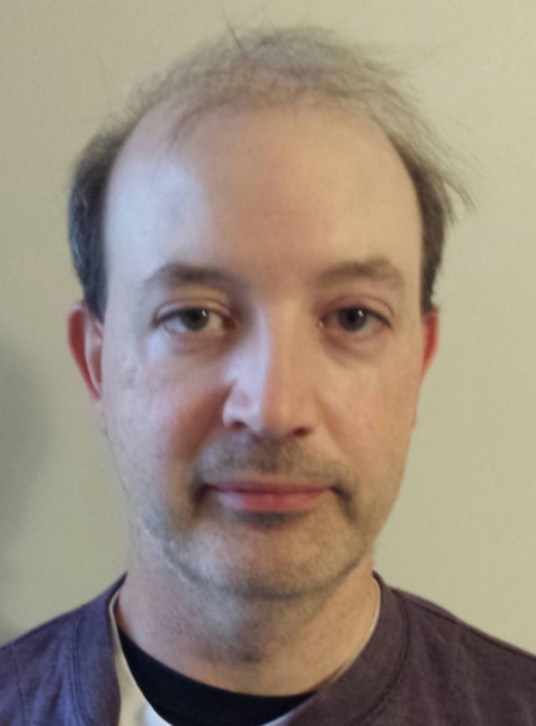 Man with dark t-shirt on light-colored background.