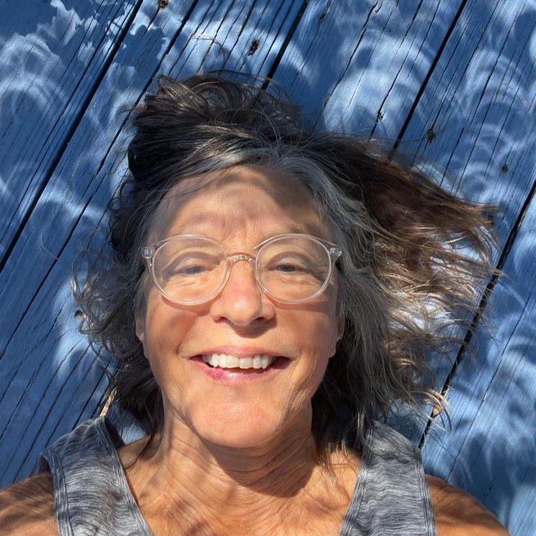 The head and shoulders of a woman lying on a wooden deck and she's covered with crescent shadows.