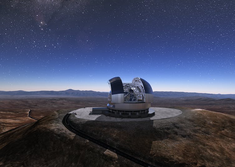 Domed observatory with roof open, in desert, under starry deep blue sky.