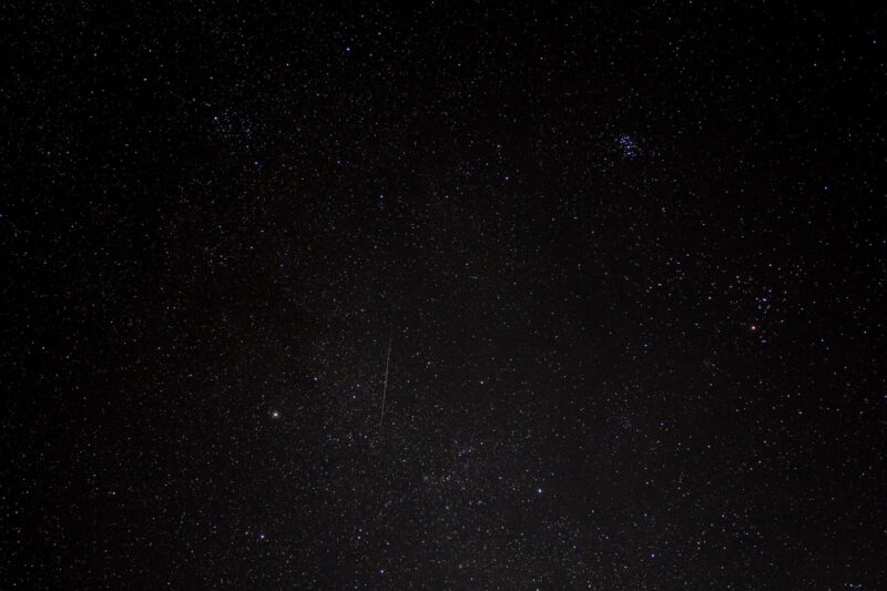 Starry dark sky with a light streak. There are some bluish stars together at the top right.