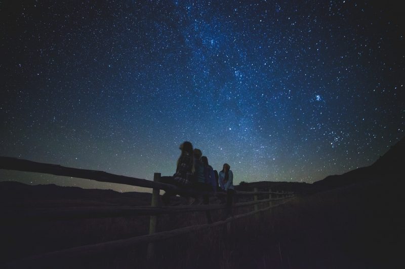 Buying a telescope: Children sit on a fence and gaze up at the stars and Milky Way.