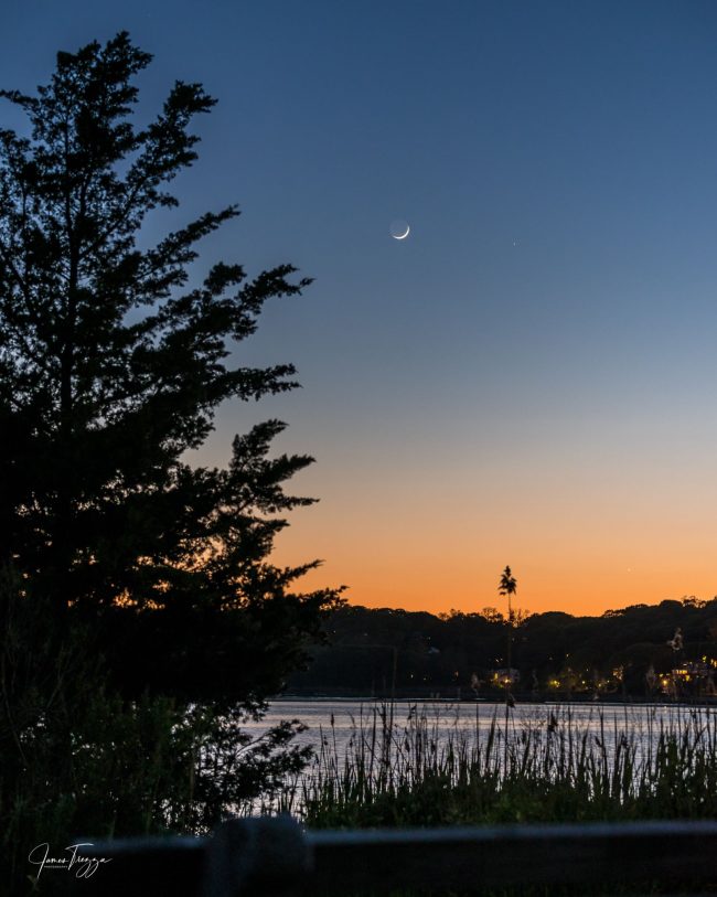 A lake shore at sunset with the moon and two bright planets.