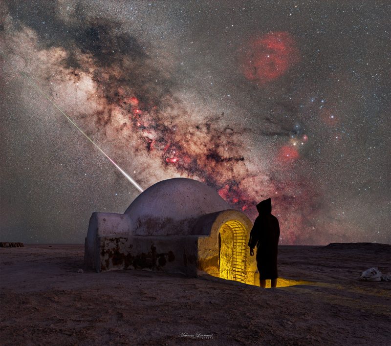 Hooded person going into igloo-like building with Milky Way in background.