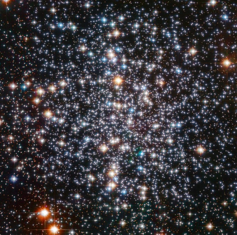 A circular scattering of very many brilliant, colorful stars in black space, less dense toward the edges.