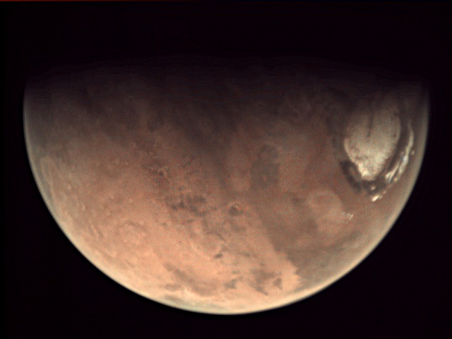 Part of Mars with its orangish surface and white polar cap against a black background.