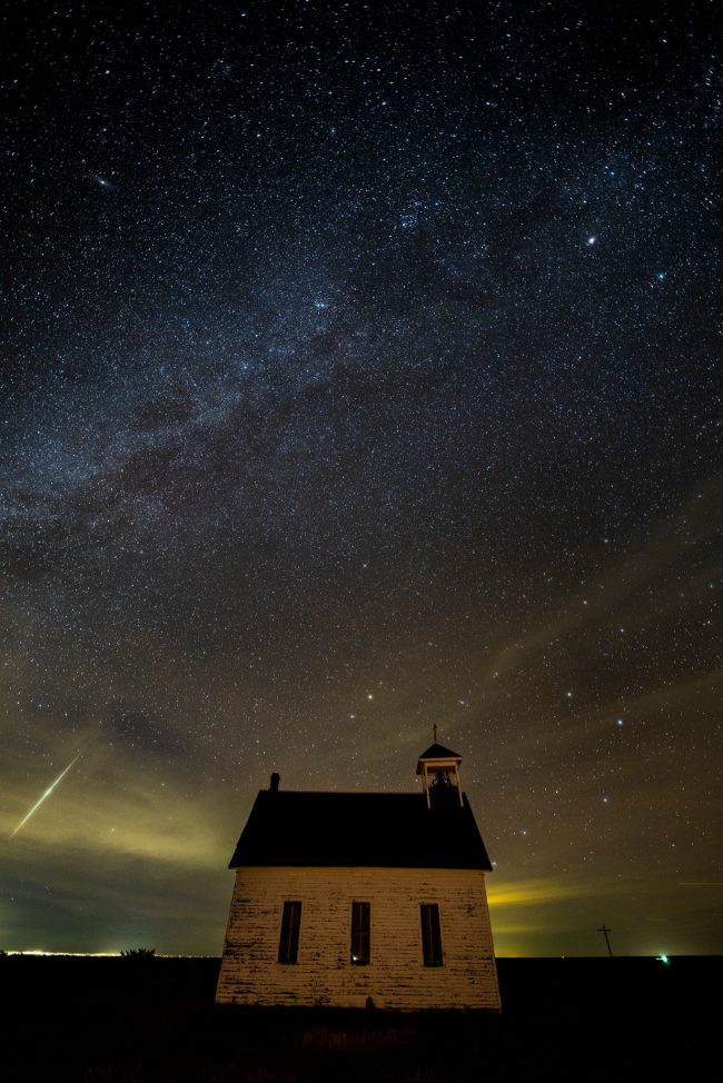 Small, old church in isolated location, dark sky, with a bright meteor.