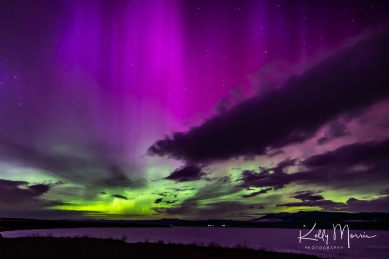 Purple and green lights over a river. The sky behind shows a few dark clouds.