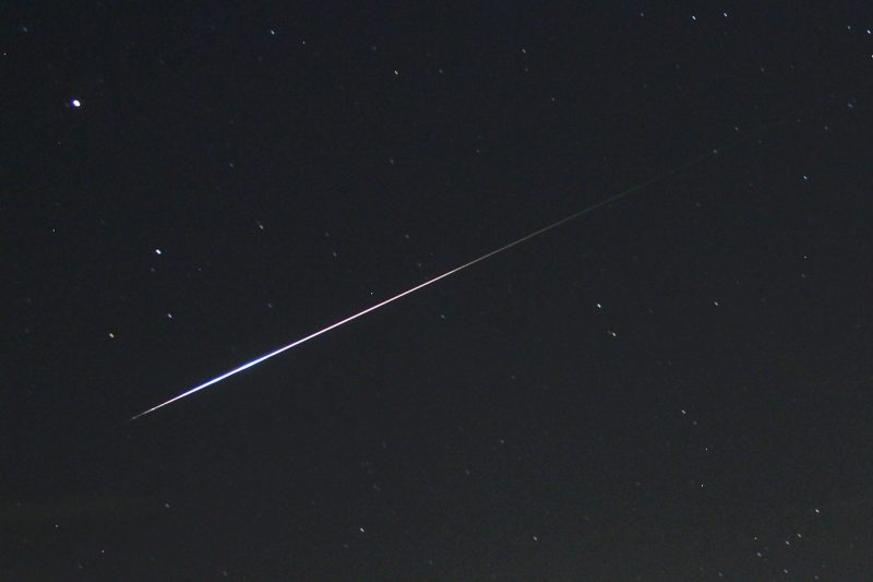 Black sky with a few scattered stars and bright streak crossing it.