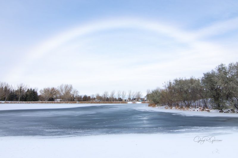 High, white fuzzy arc with very, very pale pink along the top edge, above an icy river with trees on each side.