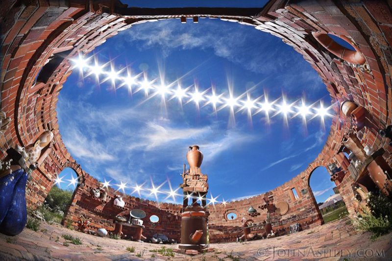 Two rows of brilliant star-like suns in a blue sky, one high and one low, through a circular open roof.