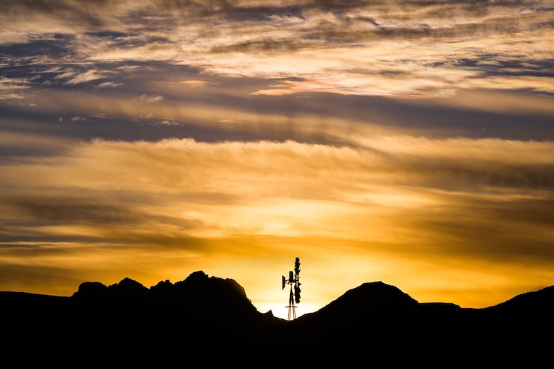 Golden sunrise with rays and clouds. A windmill and dark foreground objects.