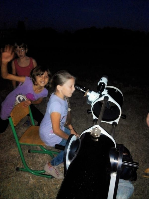 A sitting child looking in the eyepiece of a large amateur telescope, other kids waiting.