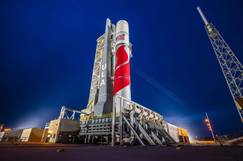 Night view of red and white rocket at launchpad, with framework towers nearby.