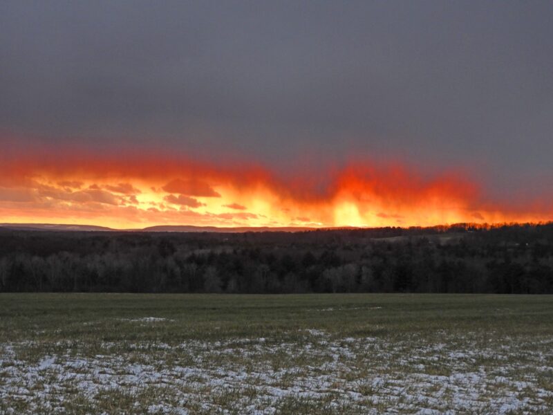 Virga: Snowy ground with orange sunset clouds on the horizon and wispy streaks stretching downward from the clouds.
