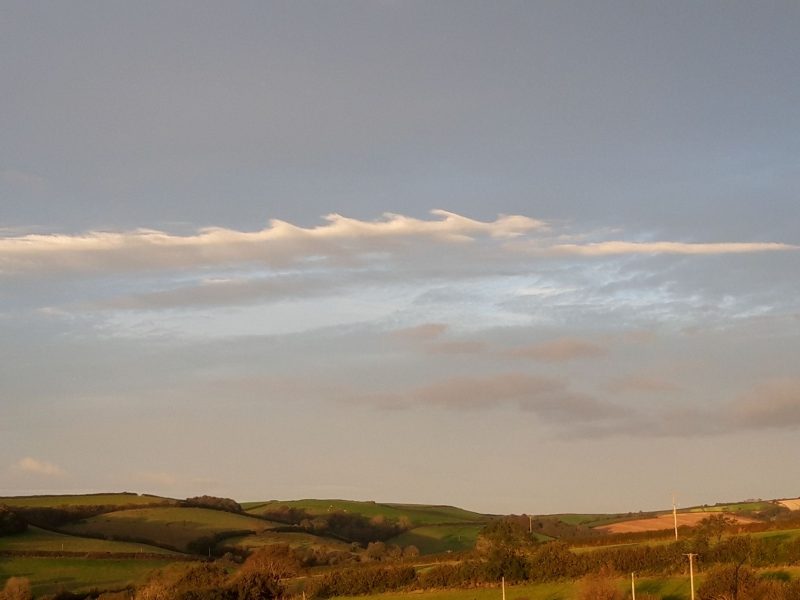 Line of high, white, wave-shaped clouds above rolling brown landscape.