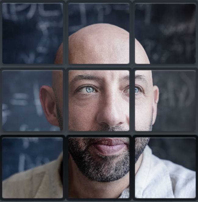 A balding man with a beard, behind a grid of black bars.