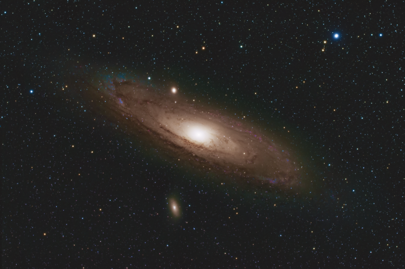 Very oblique view of fuzzy, yellowish spiral with glowing white center, dark lanes and foreground stars.